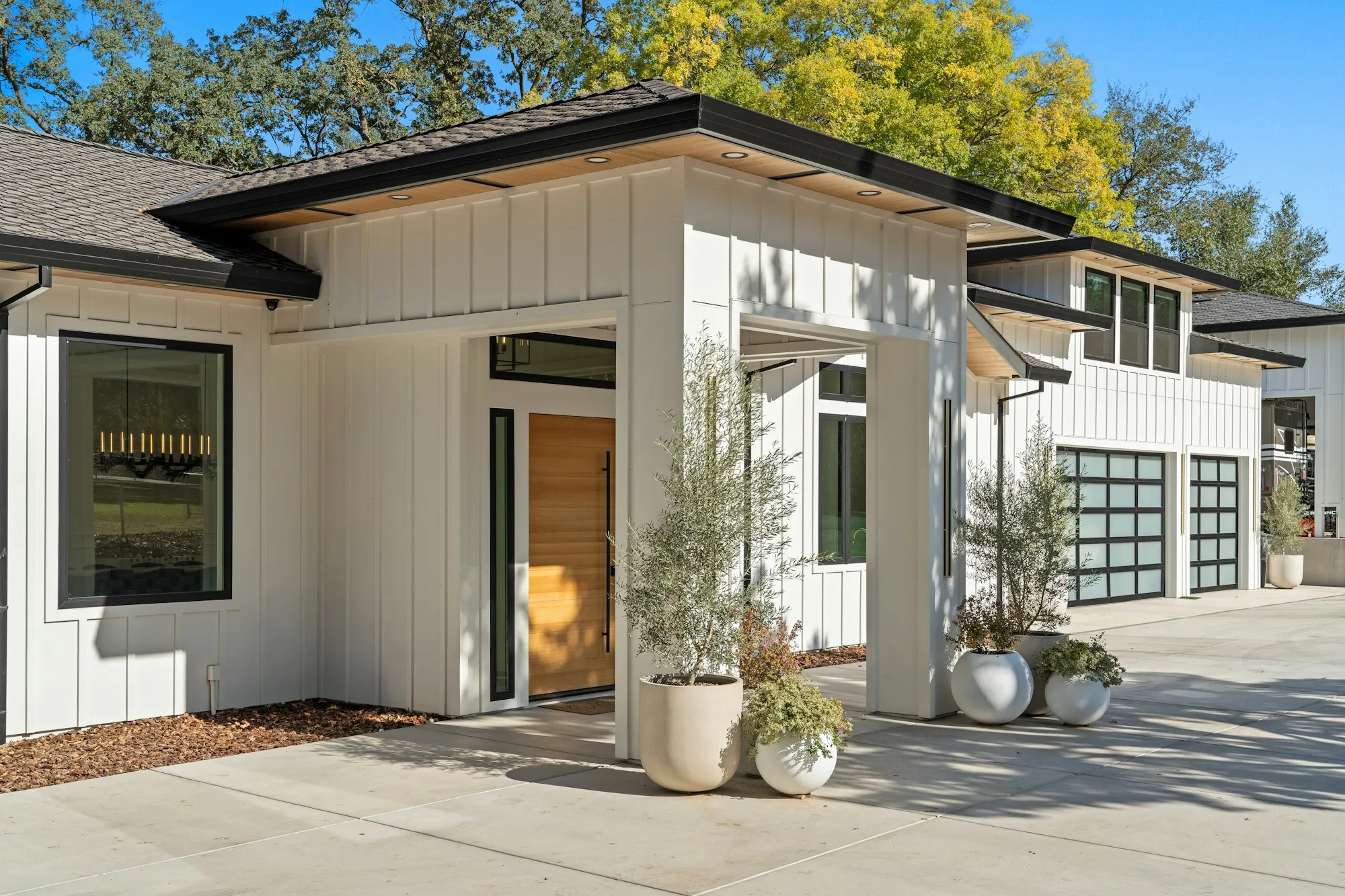 White board-and-batten house with a black-trimmed entry and potted plants